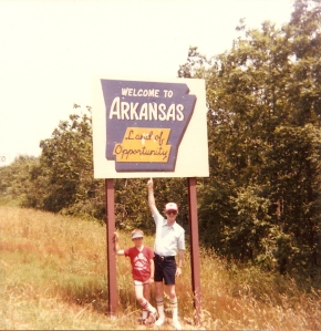 Jimmy and son standing under a "Welcome to Arkansas" sign during their "Oklahomian Exile"